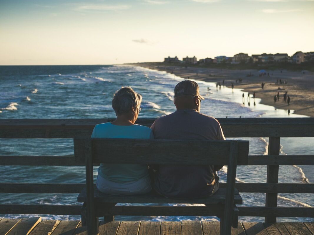 Casal sentado em um banco observando o mar, representando a aposentadoria